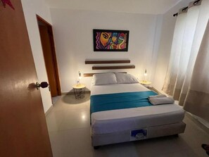 A bedroom with a bed, bedside tables, a painting, and a door. - Sweet Caribbean Hotel (San Andrés)