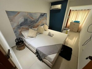 A bedroom with a bed, a headboard, a bedside table, a lamp, and a window with curtains.