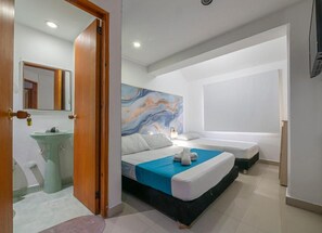 A modern hotel room with a large bed, a bedside table, a mirror, a bathroom with a sink, and a painting on the wall. - Sweet Caribbean Hotel (San Andrés)