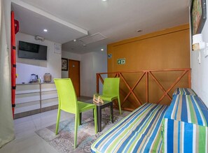 A room with a bed, two chairs, a small table, a television, and a door with an exit sign.