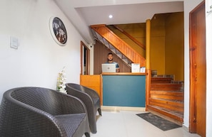 A reception area with wicker chairs, a desk, a laptop, a clock, and a staircase.