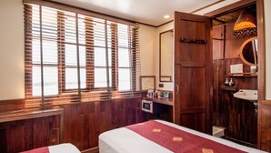 A hotel room with two beds, wooden paneling, a large window with blinds, a wooden wardrobe, a sink, and a mirror. - The Vat Phou Cruise (Pakse)
