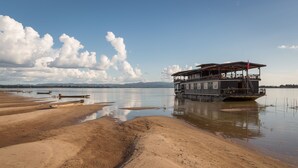 A waterfront property with a large building featuring multiple decks and a flag. - The Vat Phou Cruise (Pakse)