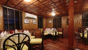 A restaurant with wooden flooring, tables with white tablecloths, and chairs with yellow cushions. - The Vat Phou Cruise (Pakse)