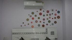 Quarto com unidade de ar condicionado branca fixada na parede, decoração de parede estampada e cama com cabeceira geométrica.