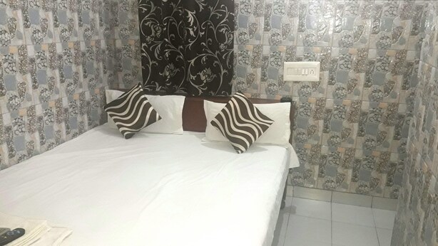 Quarto de hotel com cama, duas almofadas, um controle remoto e parede com padrão decorativo.