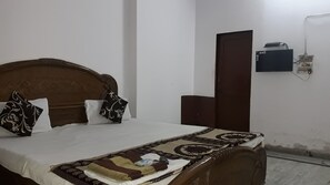 Una camera da letto con un letto di legno, cuscini bianchi e decorati, una testiera marrone, un comodino, una presa elettrica a parete e una porta.