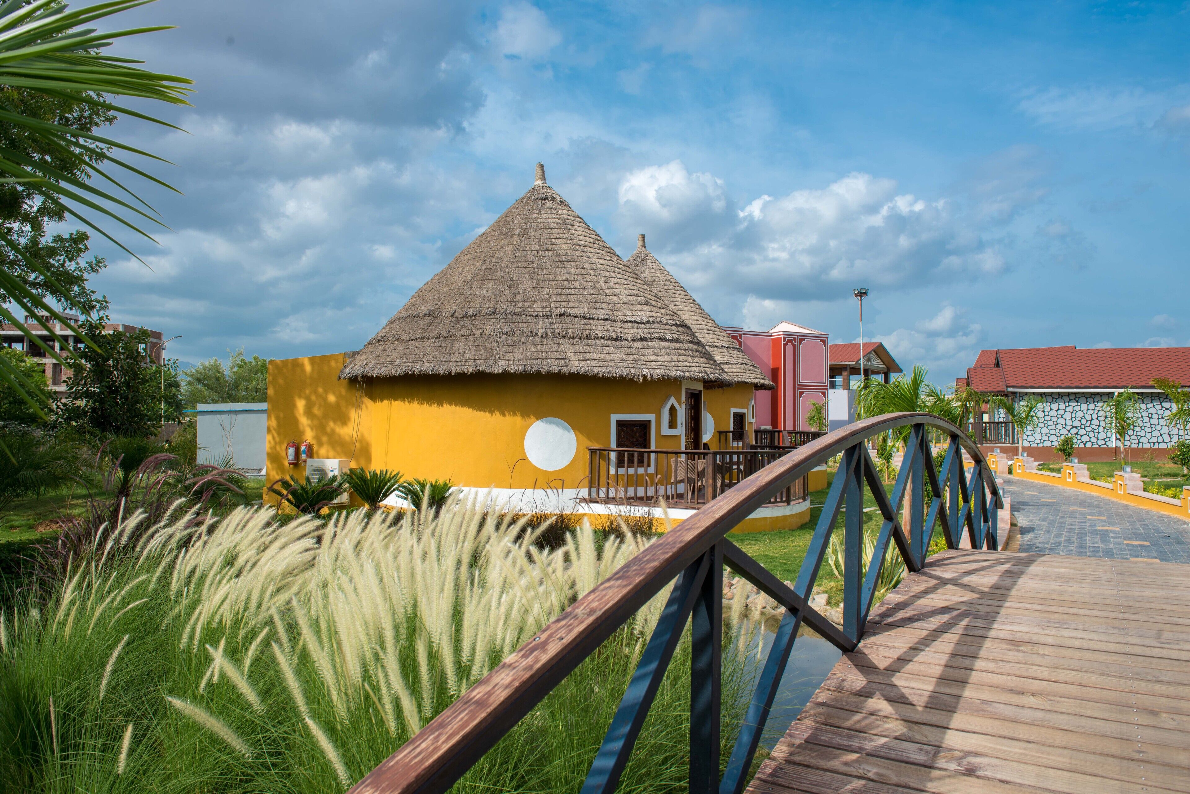 Un bâtiment jaune avec un toit de chaume, un pont en bois et un chemin pavé.