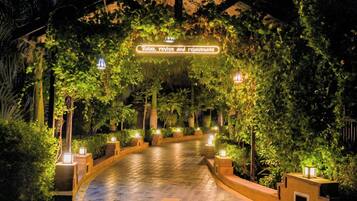 A pathway lined with plants and illuminated by lanterns, leading to a covered area with a sign that reads "Relax, revive and rejuvenate."