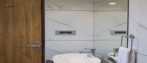A modern bathroom with a wooden door, a white marble wall, a large mirror, a white sink, and a towel rack.