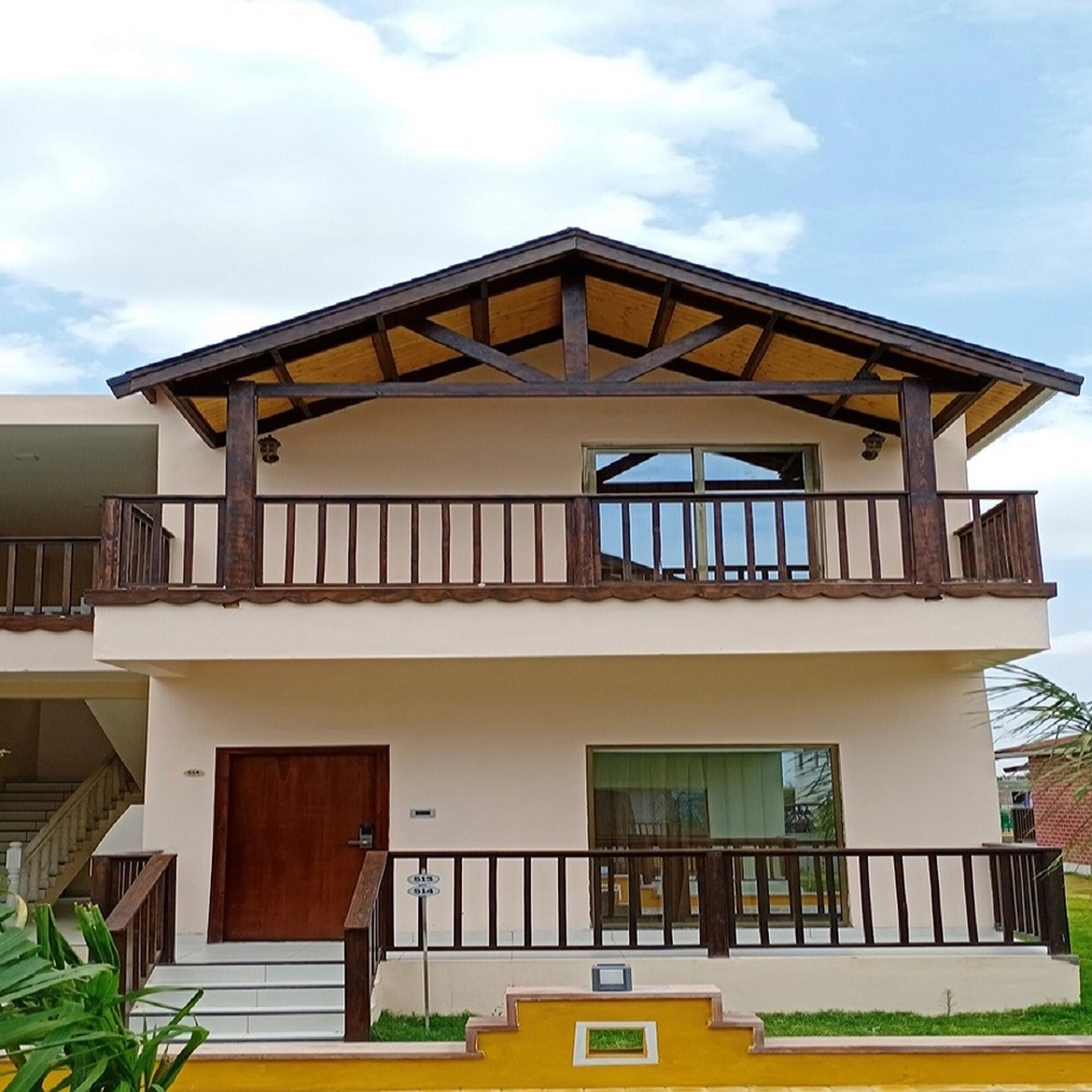 A two-story building with a balcony on the upper floor, a front door, and a staircase leading to the entrance.