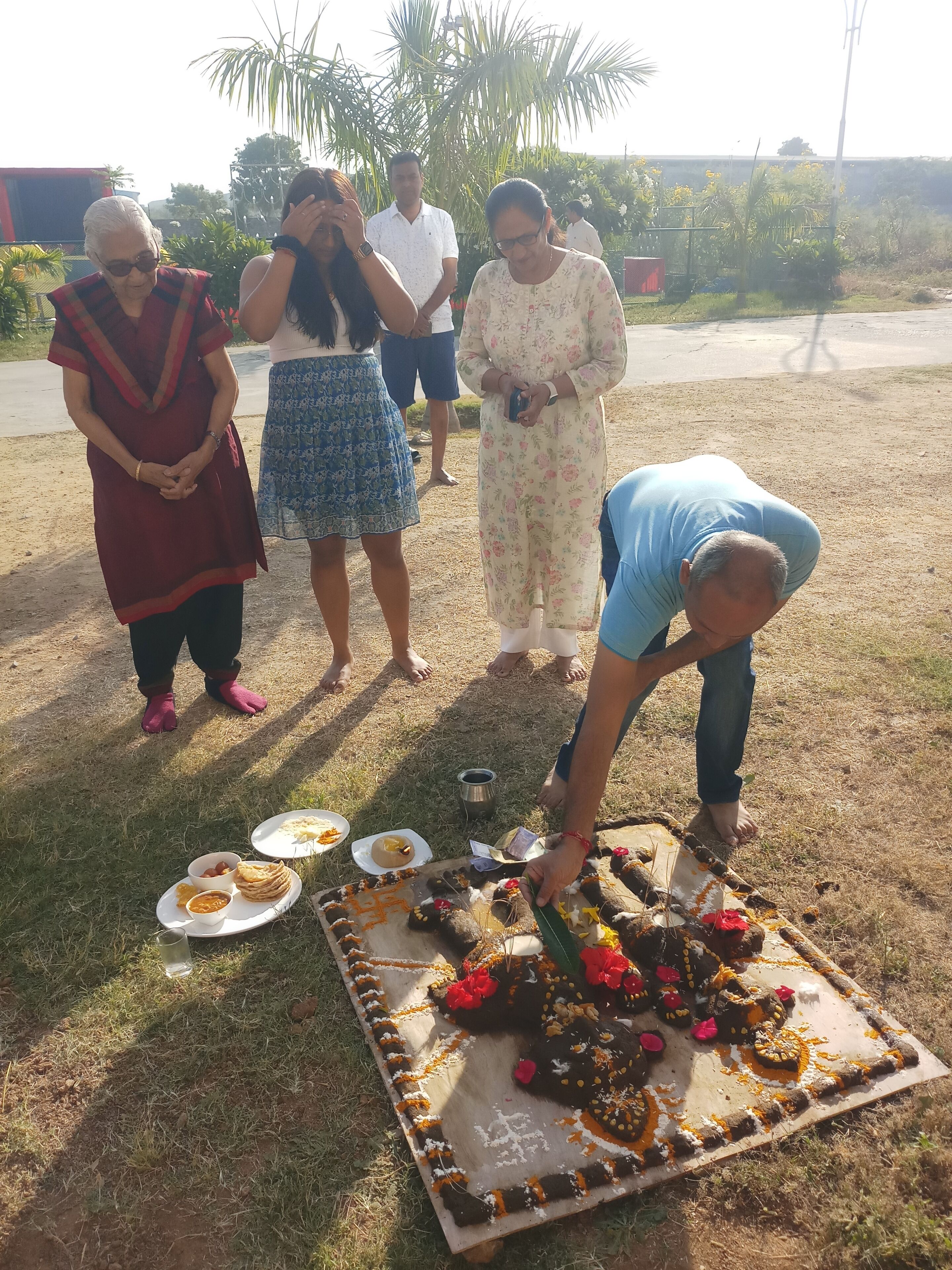 A group of people gathered around a decorated food platter outdoors.