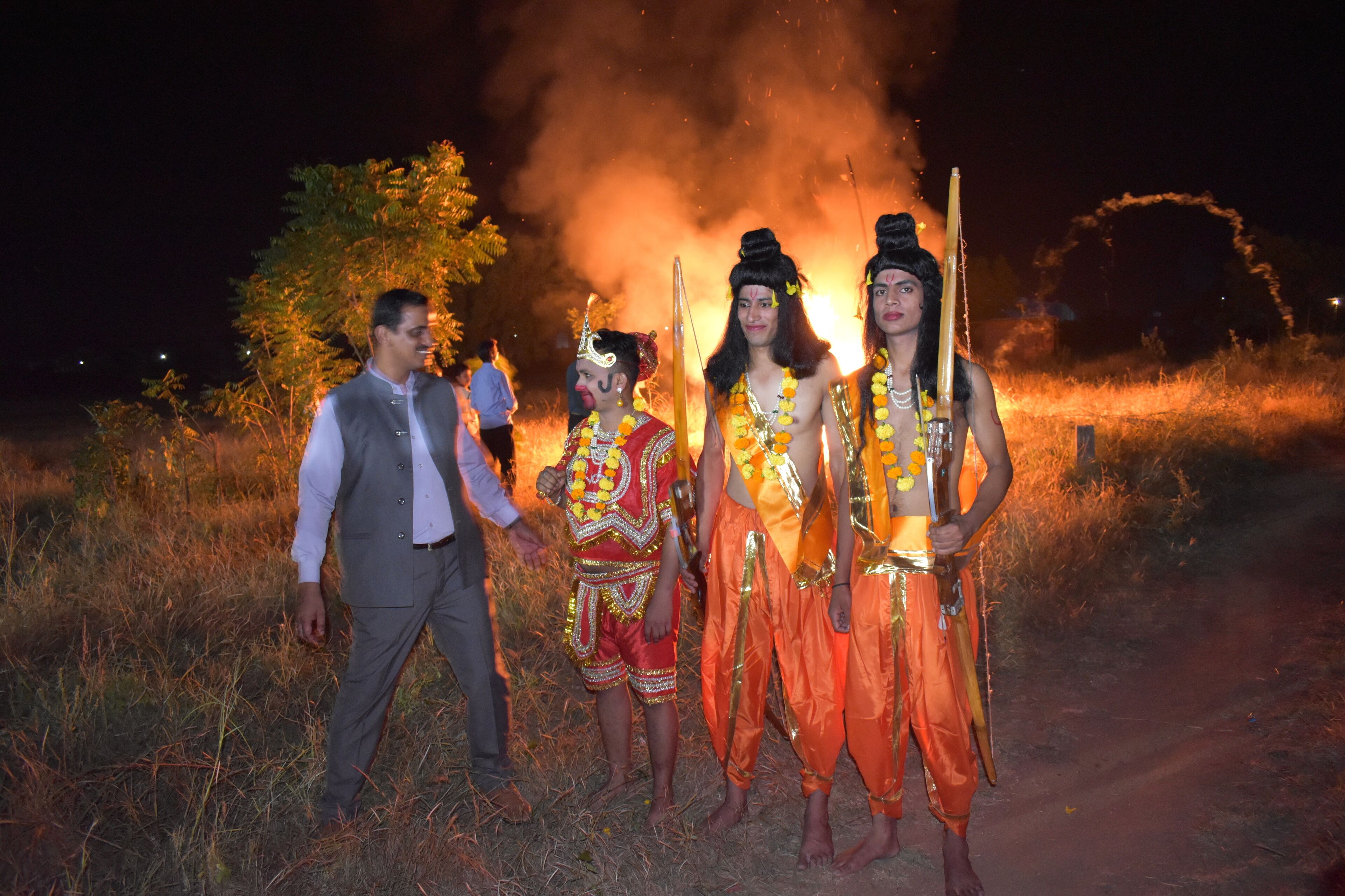 A group of people in traditional attire standing on a path with a fire in the background.