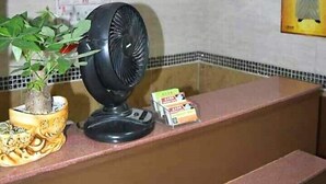 Uma área de recepção com um relógio, um ventilador, um vaso de planta e um cartaz na parede.