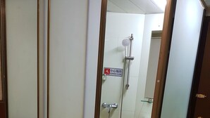 Quarto de hotel com porta de correr que dá para área de chuveiro, com aviso de piso escorregadio.