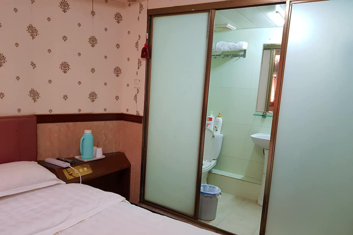 Habitación de hotel con cama, mesita de noche con lámpara, espejo, inodoro y lavabo.