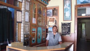 A hotel reception desk with a sign listing room types and rates, a check-out time sign, and a wall with framed pictures and documents. - Hotel Tashila - Manali (Manali)