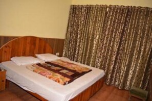 A single bed with a wooden headboard, a quilt, and a curtain. - Hotel Tashila - Manali (Manali)
