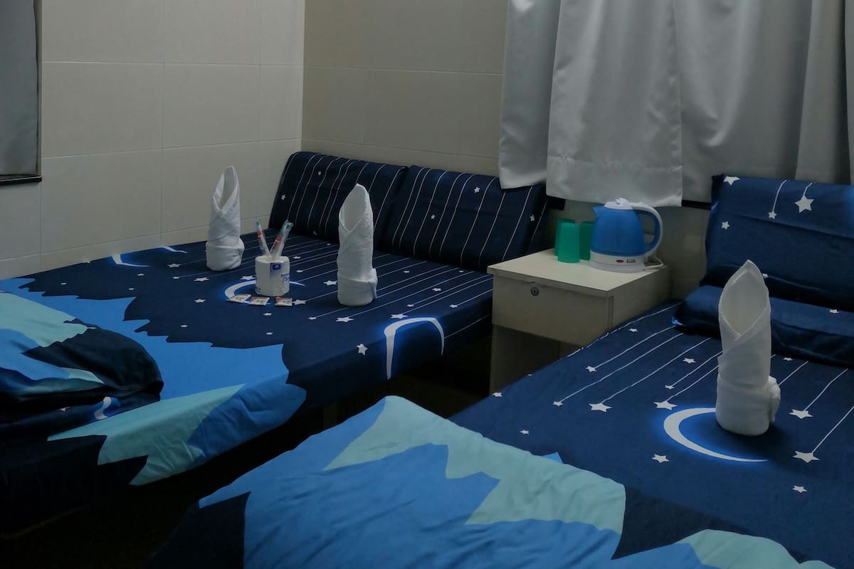 Une chambre d’hôtel avec deux lits, une petite table, un ventilateur et une fenêtre avec des rideaux.