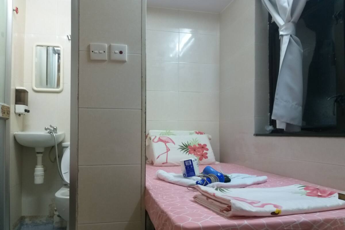 Une salle de bain avec un lavabo, des toilettes et un lit recouvert d’une courtepointe rose.