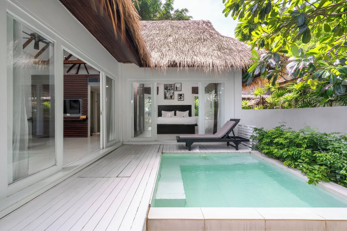 A modern villa with a pool, a thatched roof, and a balcony with a lounge chair.