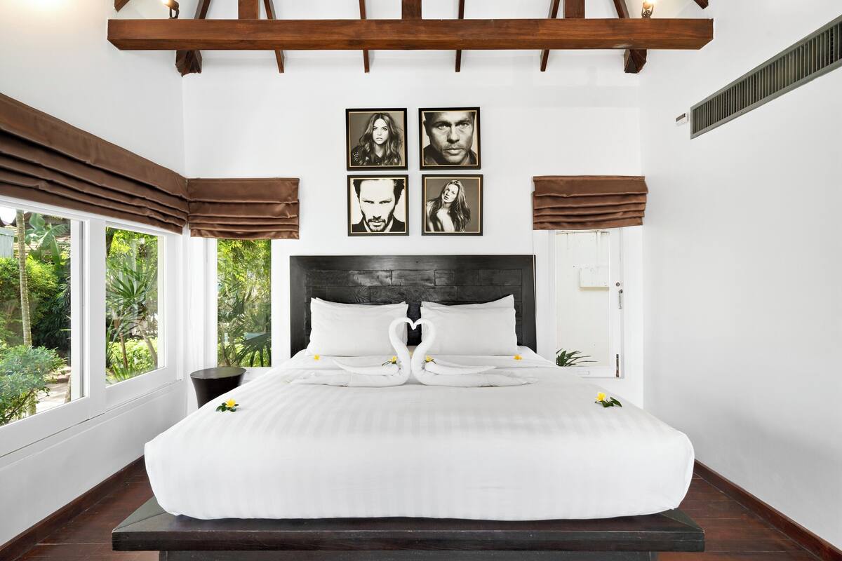 A bedroom with a large bed, a headboard with a heart-shaped towel arrangement, and four framed pictures on the wall.