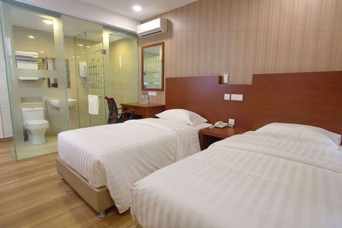 A hotel room with two beds, a glass shower enclosure, a wooden headboard, and a bedside table with a phone.