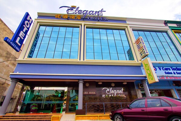 Ein Hotel mit großer Glasfassade, einem gut sichtbaren Schild mit der Aufschrift "Elegant Hotel" und einem geparkten Auto davor.