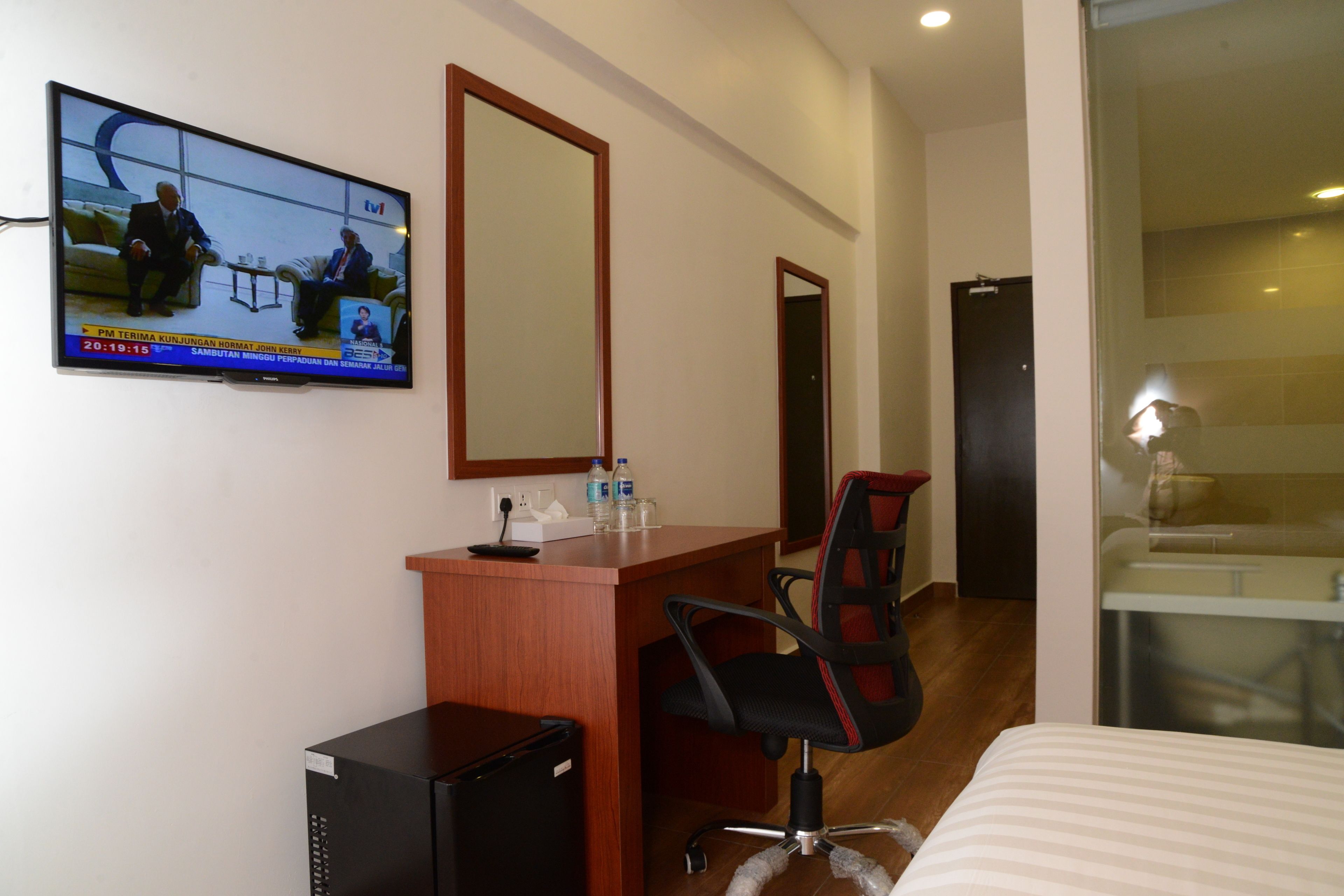 A hotel room with a TV, a desk, a chair, a bed, and a bathroom.