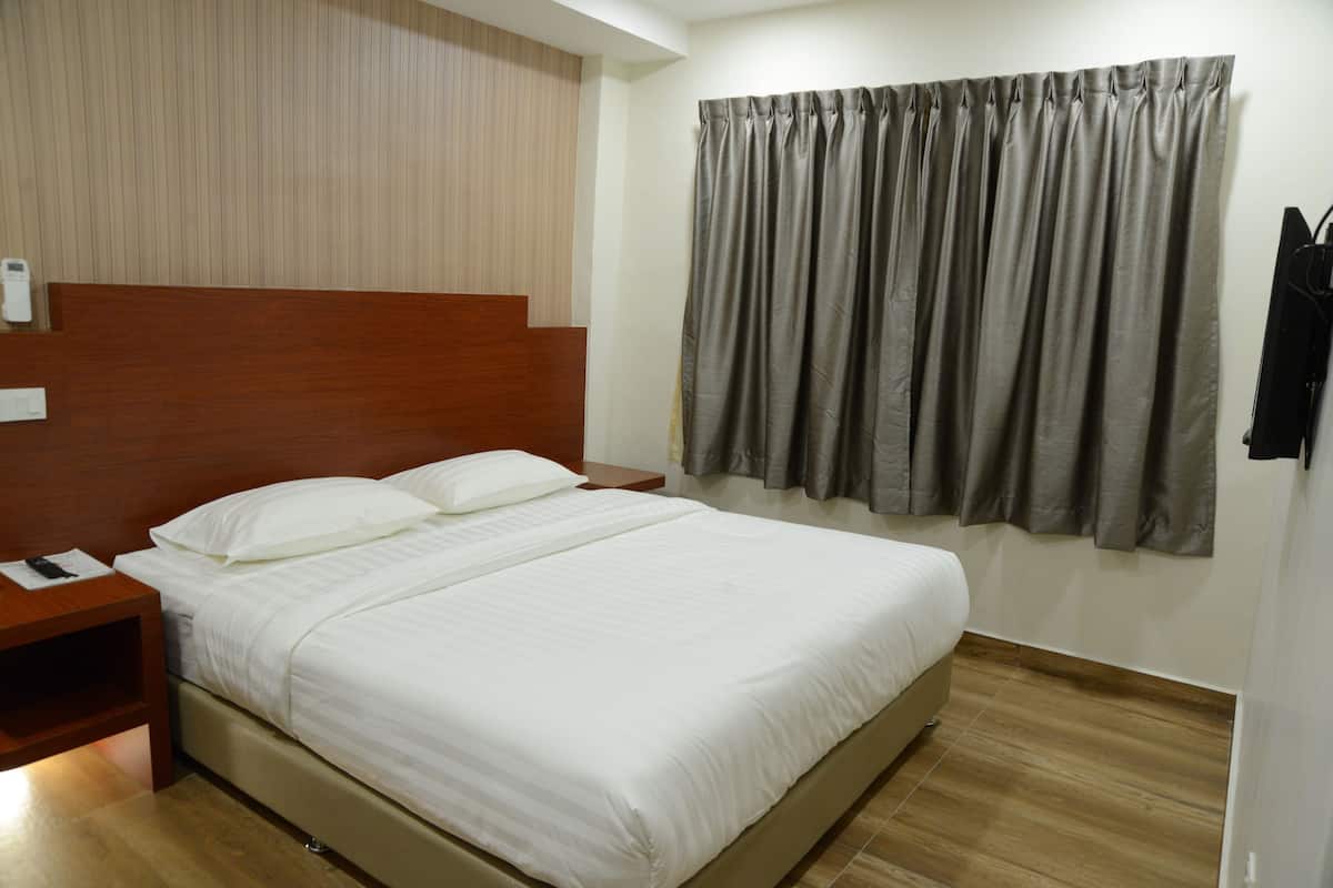 A hotel room with a bed, wooden headboard, a nightstand, a wall-mounted TV, and a curtain.