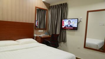 A hotel room with a bed, a desk with a chair, a television mounted on the wall, and a mirror.