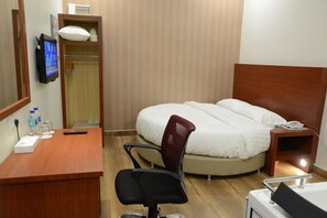 Ein Hotelzimmer mit Bett, Schreibtisch mit Stuhl, Fernseher, Nachttisch und einem Badezimmerbereich.