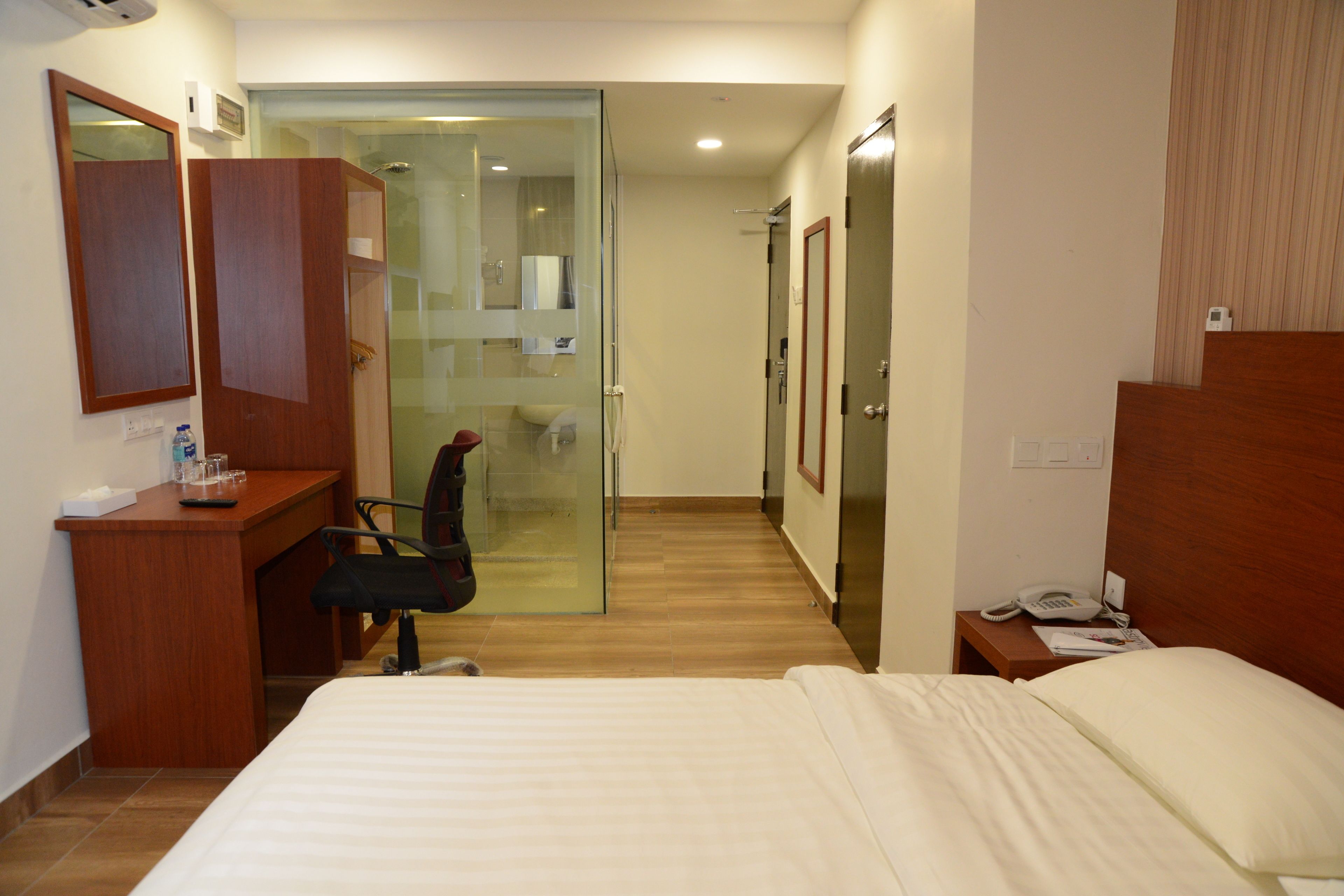 Una habitación de hotel con una cama, un escritorio con una silla, un box de ducha acristalado y un armario de madera.