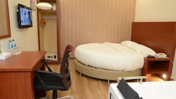 Una camera d'albergo con un letto, una scrivania, una sedia, una televisione e un comodino con un telefono.