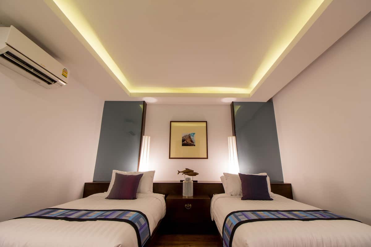 Habitación de hotel con dos camas, una mesita de noche, un cuadro en la pared y un equipo de aire acondicionado.