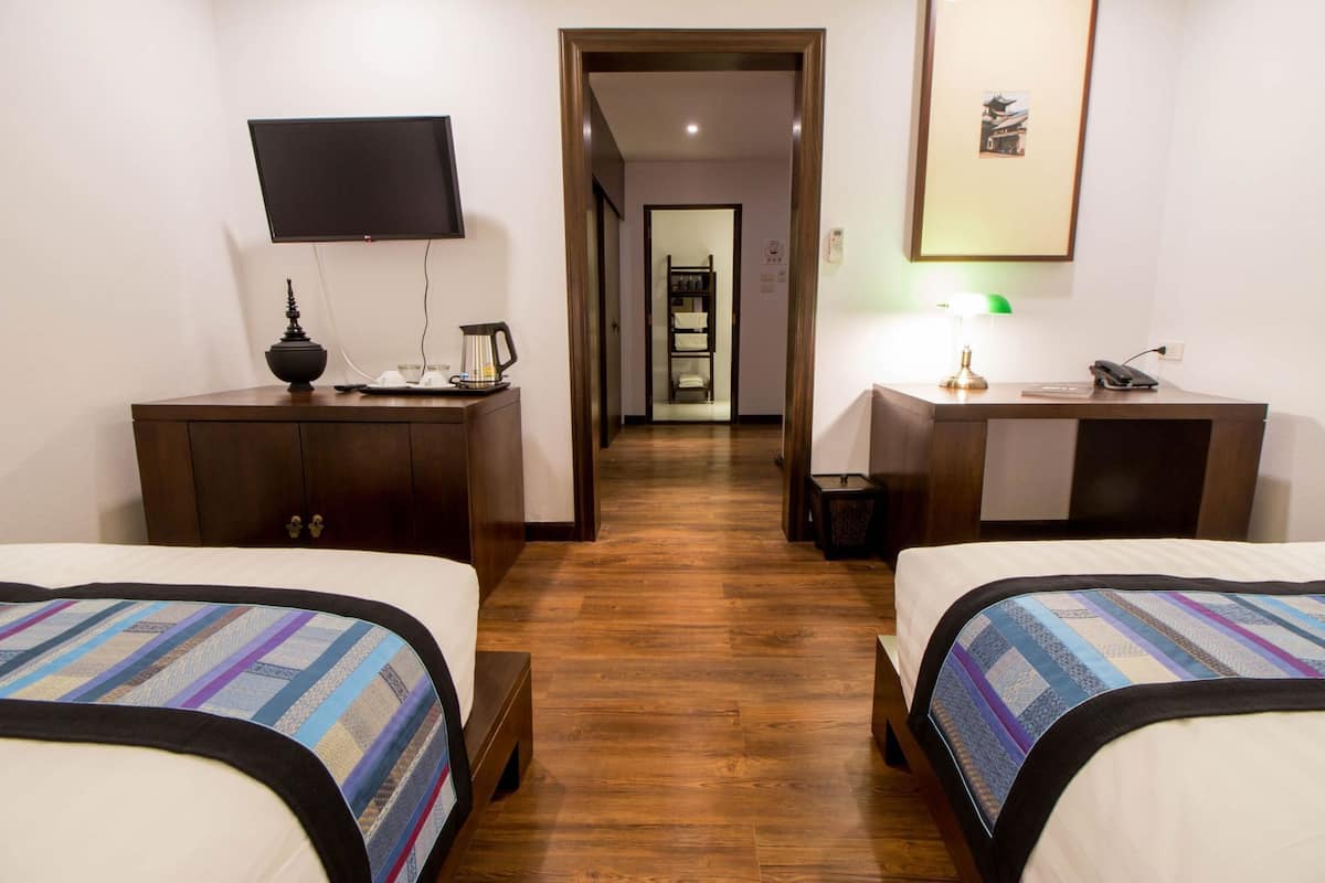Una habitación de hotel con dos camas, un escritorio, una televisión y un pasillo que conduce a un baño.
