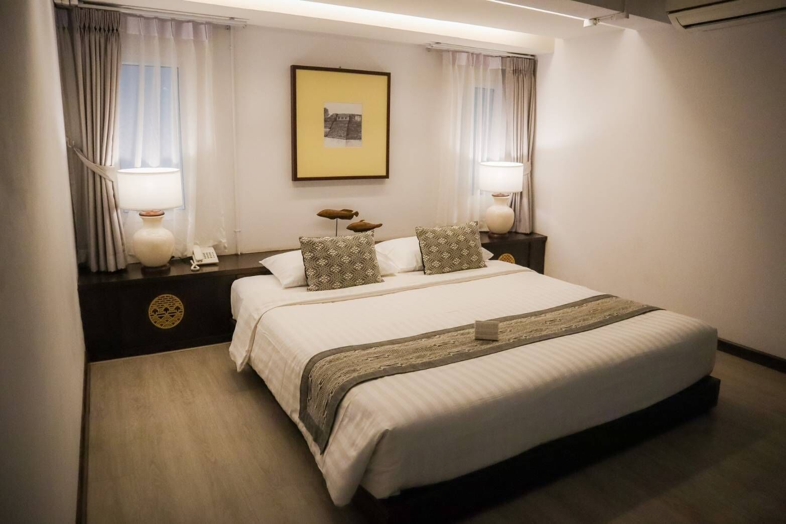 A hotel room with a large bed, two bedside tables with lamps, a framed picture on the wall, and a window with curtains.