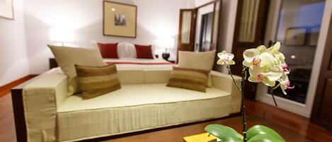 A modern hotel room with a sofa bed, a small table with a plant and a book, and a window with curtains.