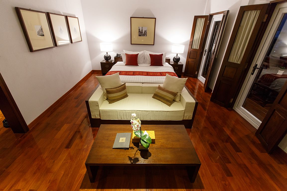 A hotel room with a bed, a sofa, a coffee table with a book and a vase, and framed pictures on the wall.