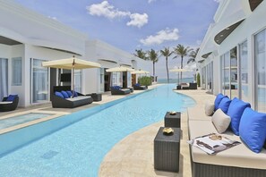 A poolside area with lounge chairs and umbrellas, a clear blue pool, and a view of the ocean.