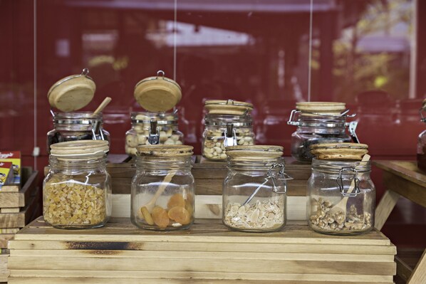 A display of glass jars with lids containing various food items like nuts, dried fruits, and oats, arranged on wooden crates.
