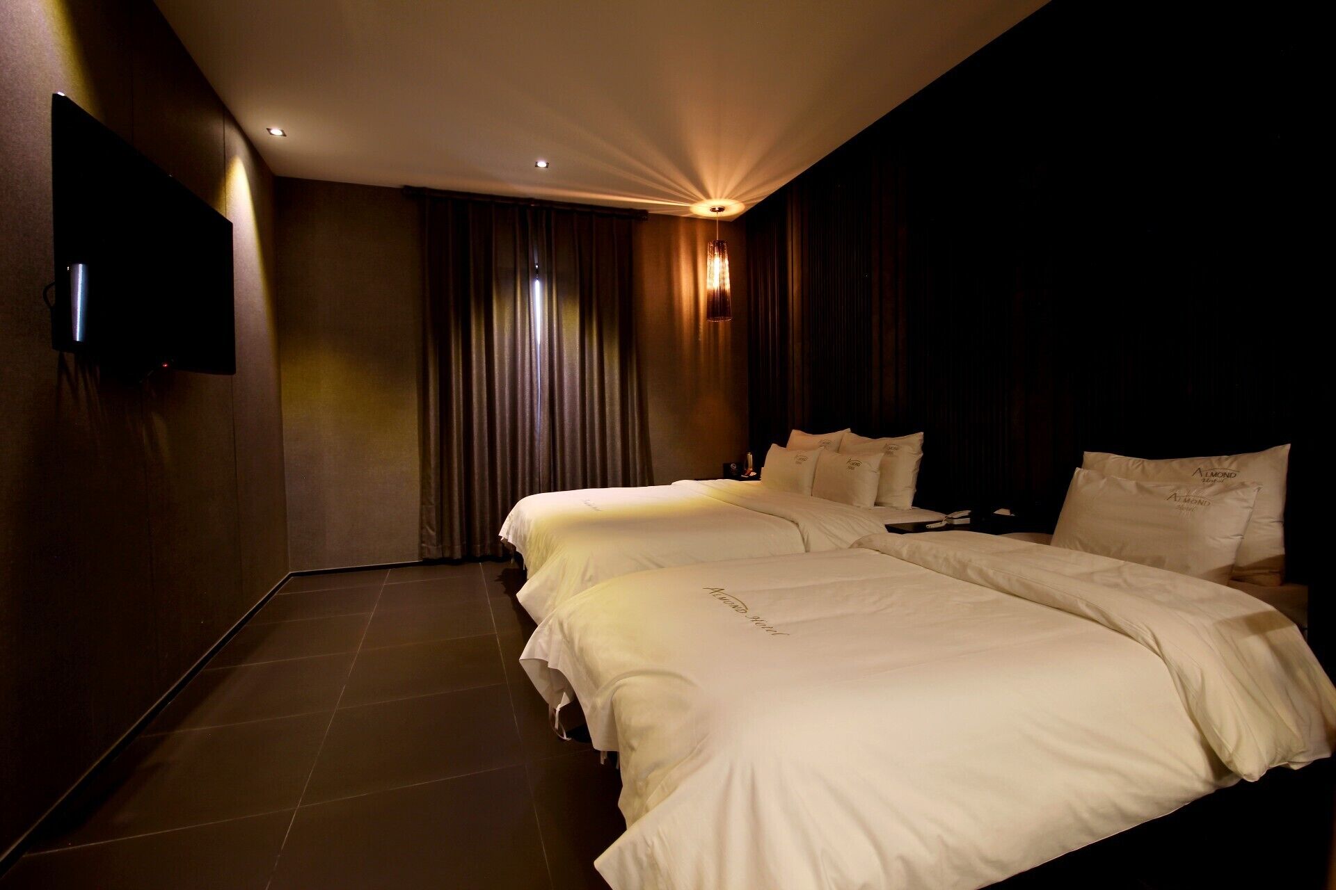 A hotel room with a large bed, a flat-screen TV mounted on the wall, and a chandelier.