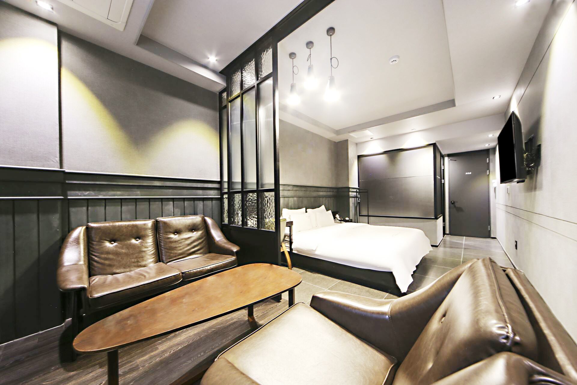 A modern hotel room with a large bed, a seating area with a sofa and chairs, a small table, and a TV mounted on the wall.