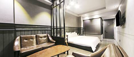 A modern hotel room with a large bed, a seating area with a sofa and chairs, a small table, and a TV mounted on the wall.