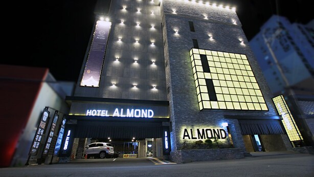 A hotel with a modern facade, illuminated signage, and a car parked in front. - Masan Almond Hotel (Changwon)