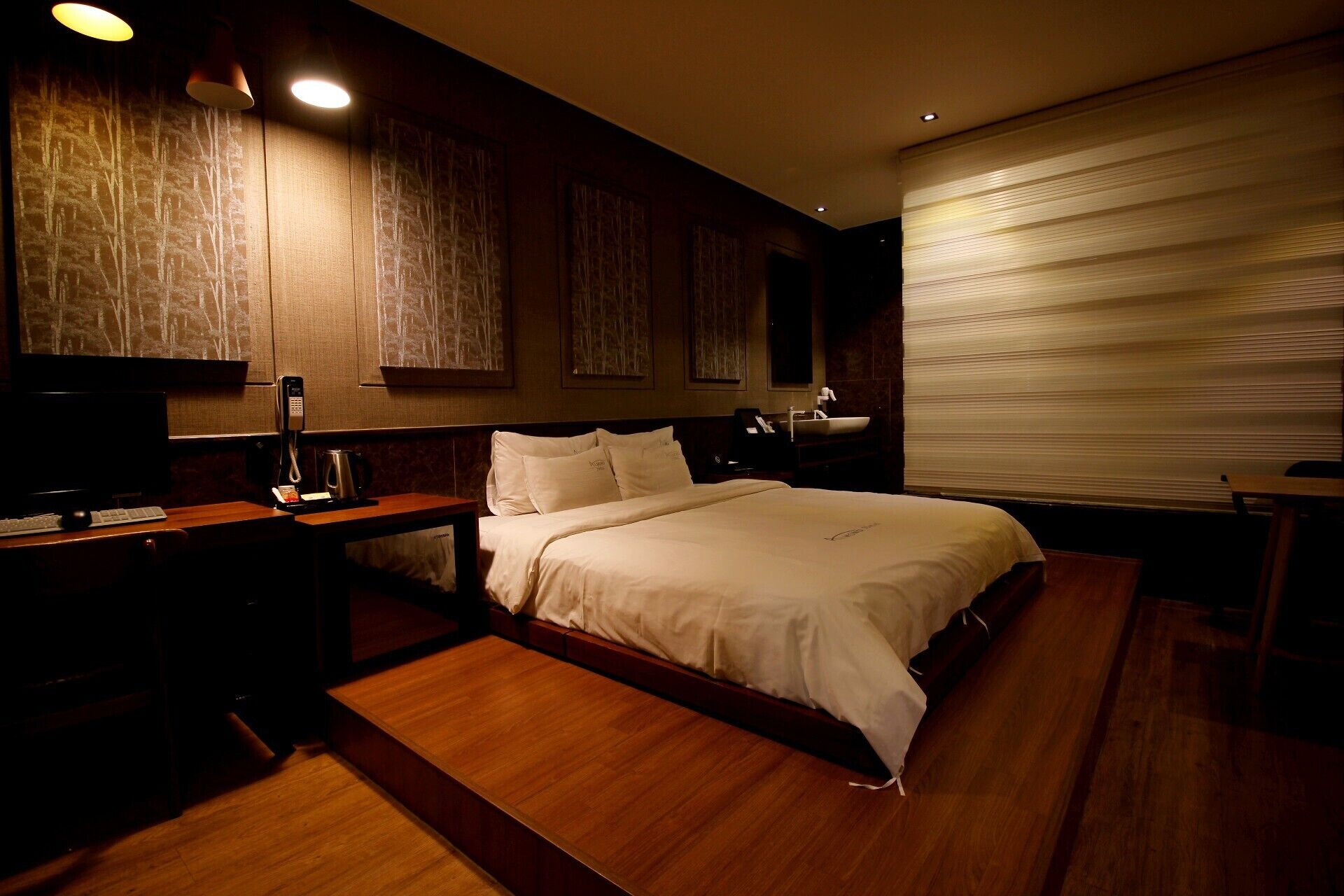 A hotel room with a large bed, a desk with a computer, a telephone, and a small table.