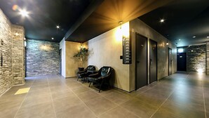 A modern hotel lobby with a stone wall, a reception desk, and numbered doors leading to guest rooms. - Masan Almond Hotel (Changwon)