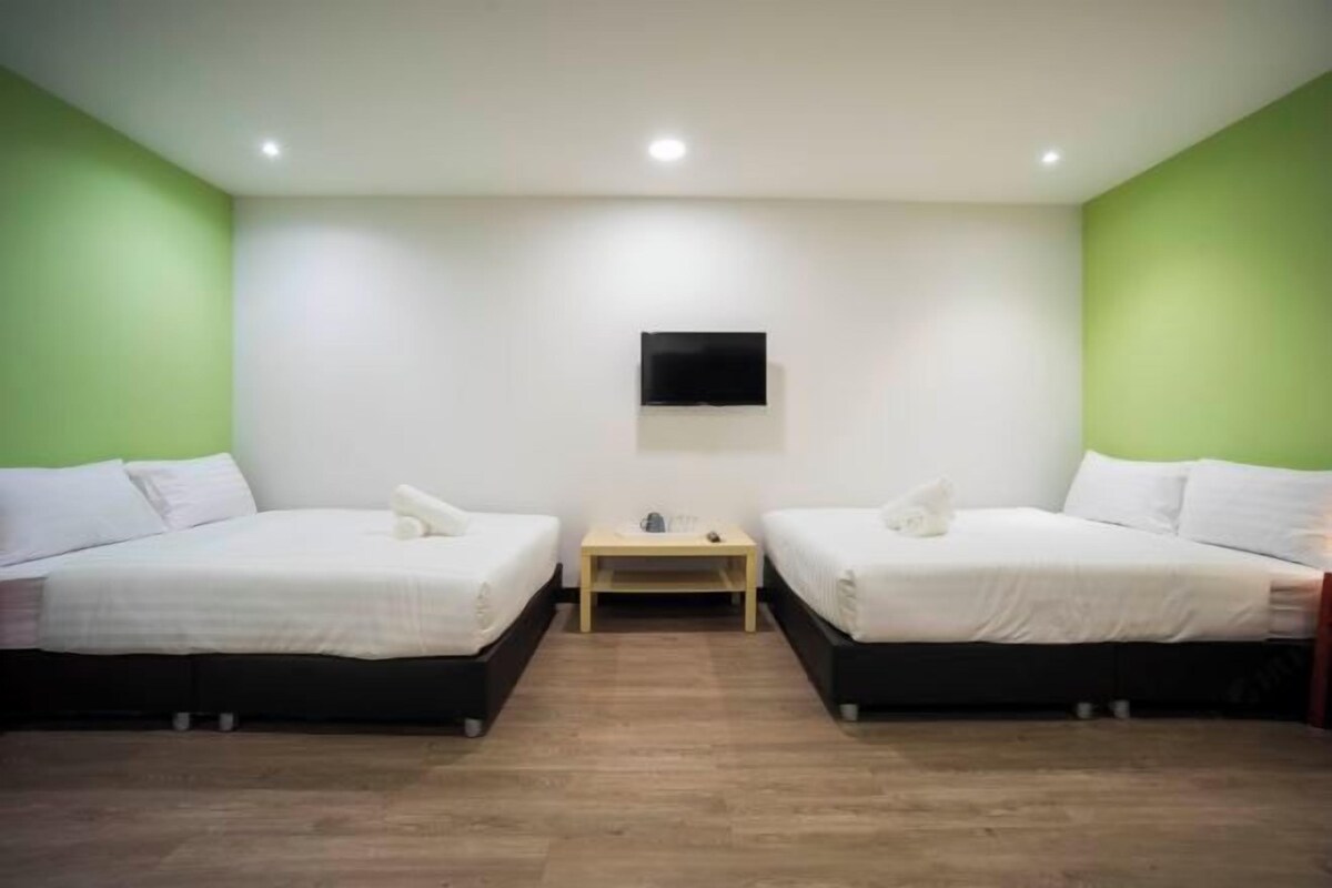 Een kamer met twee bedden, een tafeltje, een wandtelevisie en groene wanden.