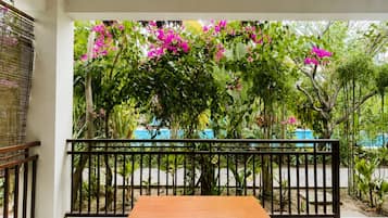 A wooden table with four chairs, a red object on the table, and a view of a garden with pink flowers and a black railing.