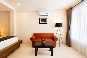 Una habitación de hotel con cama, sofá, una mesita, lámpara de pie y equipo de aire acondicionado.